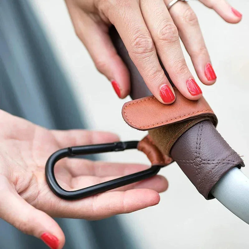 Dettaglio gancio passeggino pelle PU rosa con moschettone nero tenuto in mano
