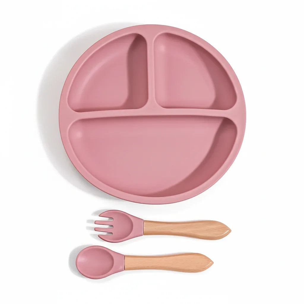 Piattino diviso in silicone rosa con cucchiaio e forchetta manico legno sfondo bianco