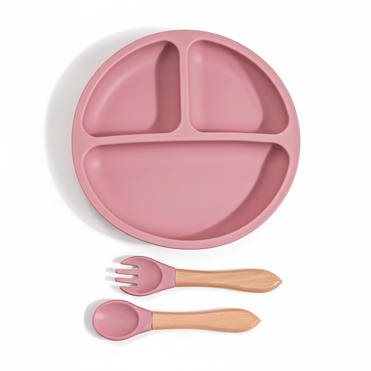 Piattino diviso in silicone rosa con cucchiaio e forchetta manico legno sfondo bianco